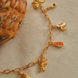 A gold-plated chain link charm bracelet with a turtle, jaguar, papaya, banana, and monkey charms.