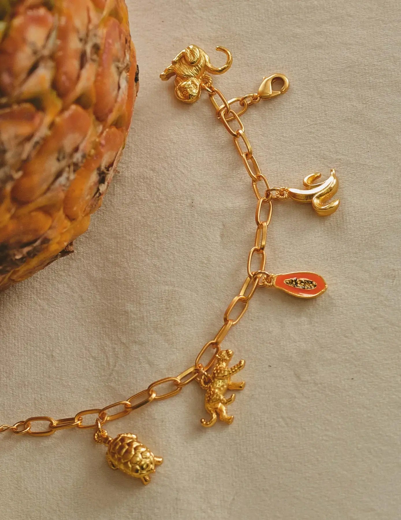 A gold-plated chain link charm bracelet with a turtle, jaguar, papaya, banana, and monkey charms.