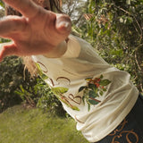 Woman wearing a beige t-shirt for 'Colombia' standing in a forest.