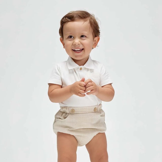 A baby wearing a white soft cotton polo shirt and beige shorts with a faux pocket, standing against a white background.