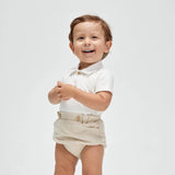 A baby wearing a white soft cotton polo shirt and beige shorts with a faux pocket, standing against a white background.