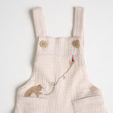A close-up a beige short-sleeved overall with bear embroidery on the front, standing against a white background.