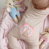 Close-up of a beige short-sleeve cotton onesie with a hand-embroidered ladybug on the chest and a matching applique on the bottom.