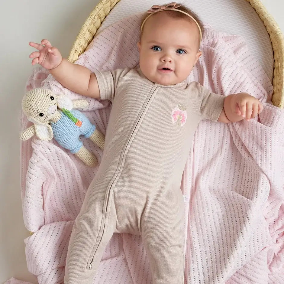 A baby wearing a beige short-sleeve cotton onesie with a hand-embroidered ladybug on the chest and a matching applique on the bottom.