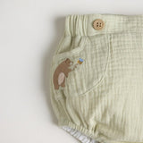 A light green diaper cover with wooden button accents and a embroidered bear detail.