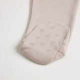 A close-up of a beige short-sleeve cotton onesie with a hand-embroidered hedgehog on the chest and a matching applique on the bottom, lying on a similar colored fabric.