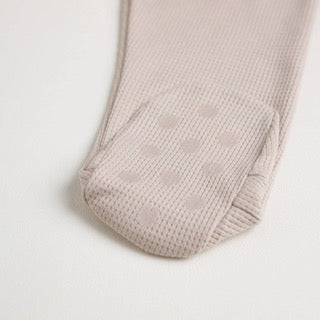 A close-up of a beige short-sleeve cotton onesie with a hand-embroidered hedgehog on the chest and a matching applique on the bottom, lying on a similar colored fabric.