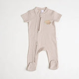 A close-up of a beige short-sleeve cotton onesie with a hand-embroidered hedgehog on the chest and a matching applique on the bottom, lying on a similar colored fabric.