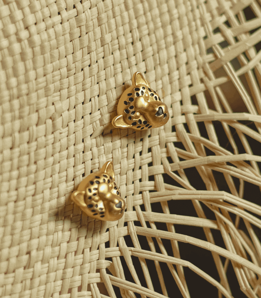 A close-up of gold-plated jaguar earring set, placed on a woven straw surface.