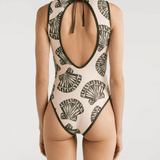 A model wearing a beige one-piece swimsuit with a nature-inspired shell print, featuring a high neckline and an open back with a tie closure.