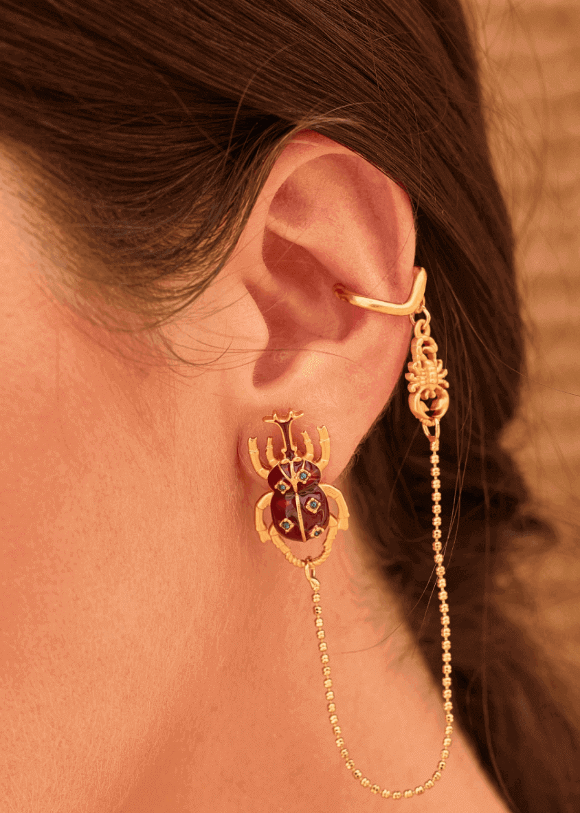 Gold ear cuff with beetle design and chain detail worn by a person.
