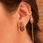 Gold ear cuff with beetle design and chain detail worn by a person.