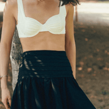 A model wearing a white underwire ruffled bikini top with a pleated black flared mini skirt.