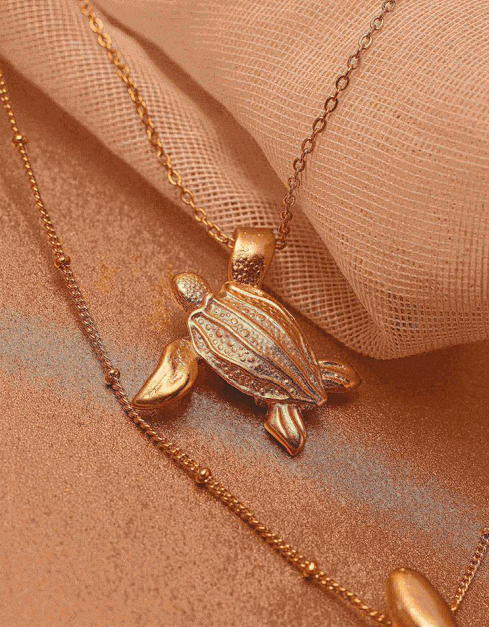 Gold turtle pendant necklace on a soft fabric background.