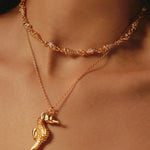 Close-up of gold necklace with seahorse pendant on a person's neck.