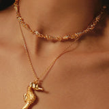 Close-up of gold necklace with seahorse pendant on a person's neck.