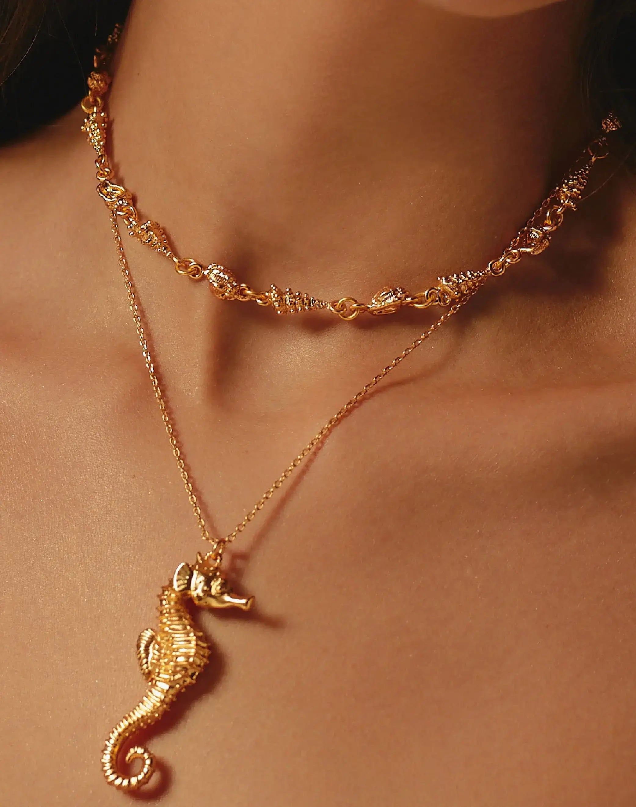 Close-up of gold necklace with seahorse pendant on a person's neck.