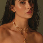 Woman wearing a gold necklace with a seahorse pendant against a neutral background.