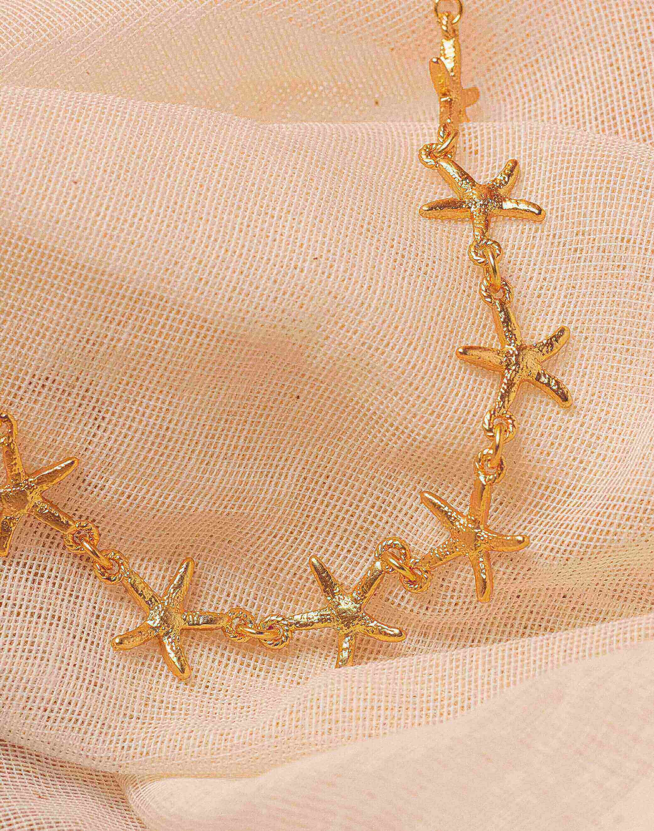 Gold starfish necklace on a beige fabric background.