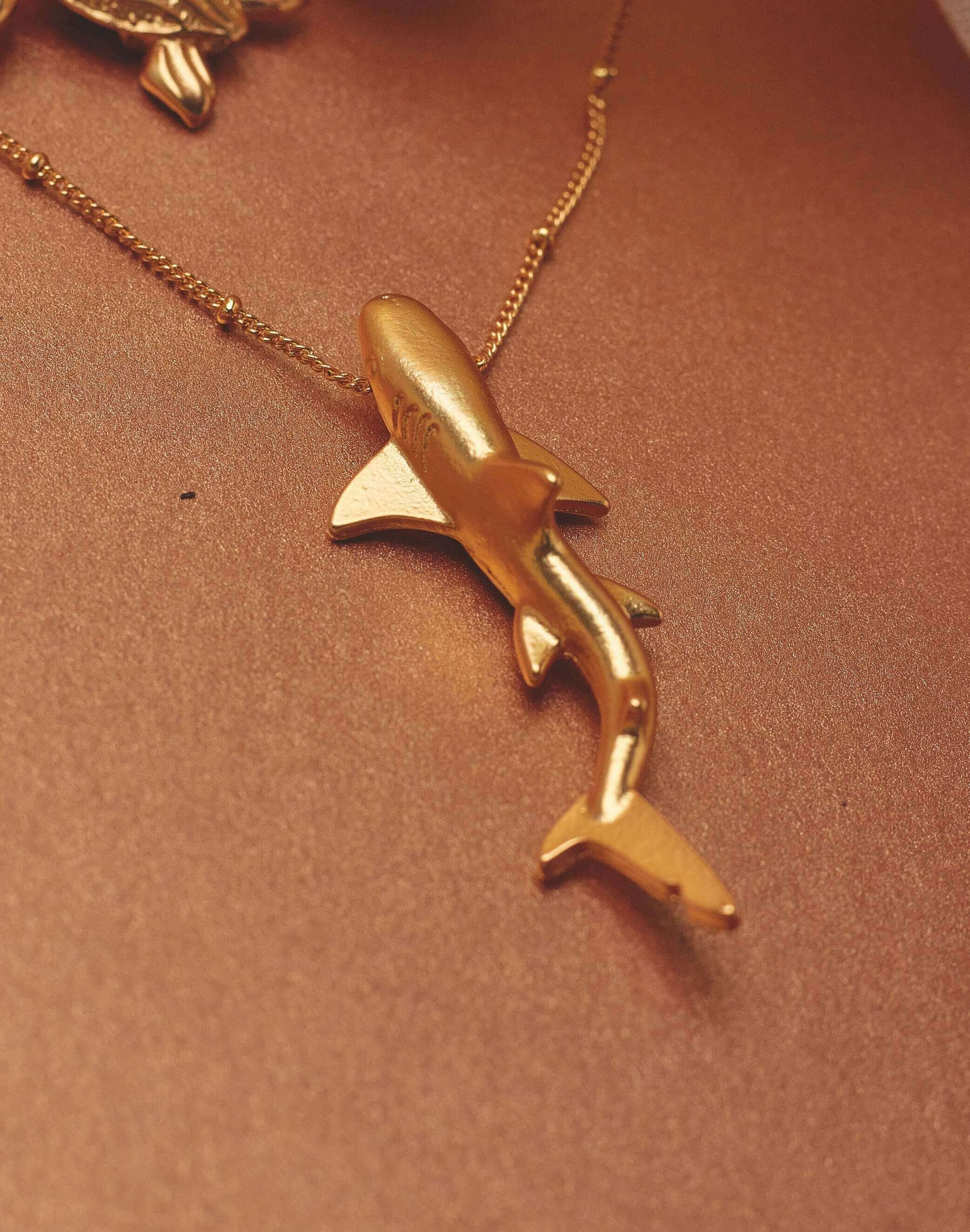 Gold shark-shaped pendant on a chain against a brown background.