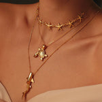 Close-up of a person wearing gold necklaces with turtle, starfish and shark designs.