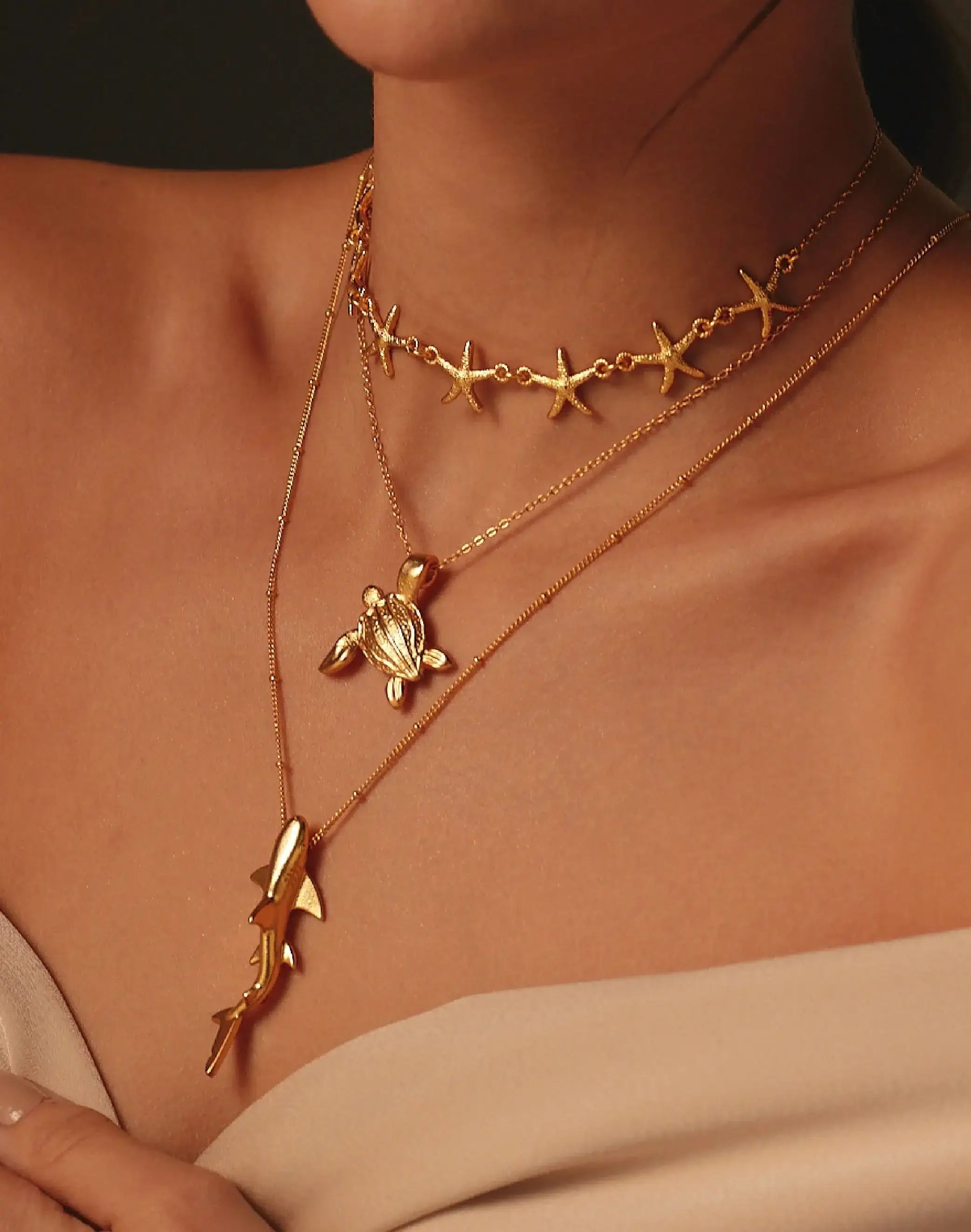 Close-up of a person wearing gold necklaces with turtle, starfish and shark designs.