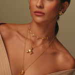 Woman wearing gold necklace set with starfish, turtles and shark pendant against a neutral background.
