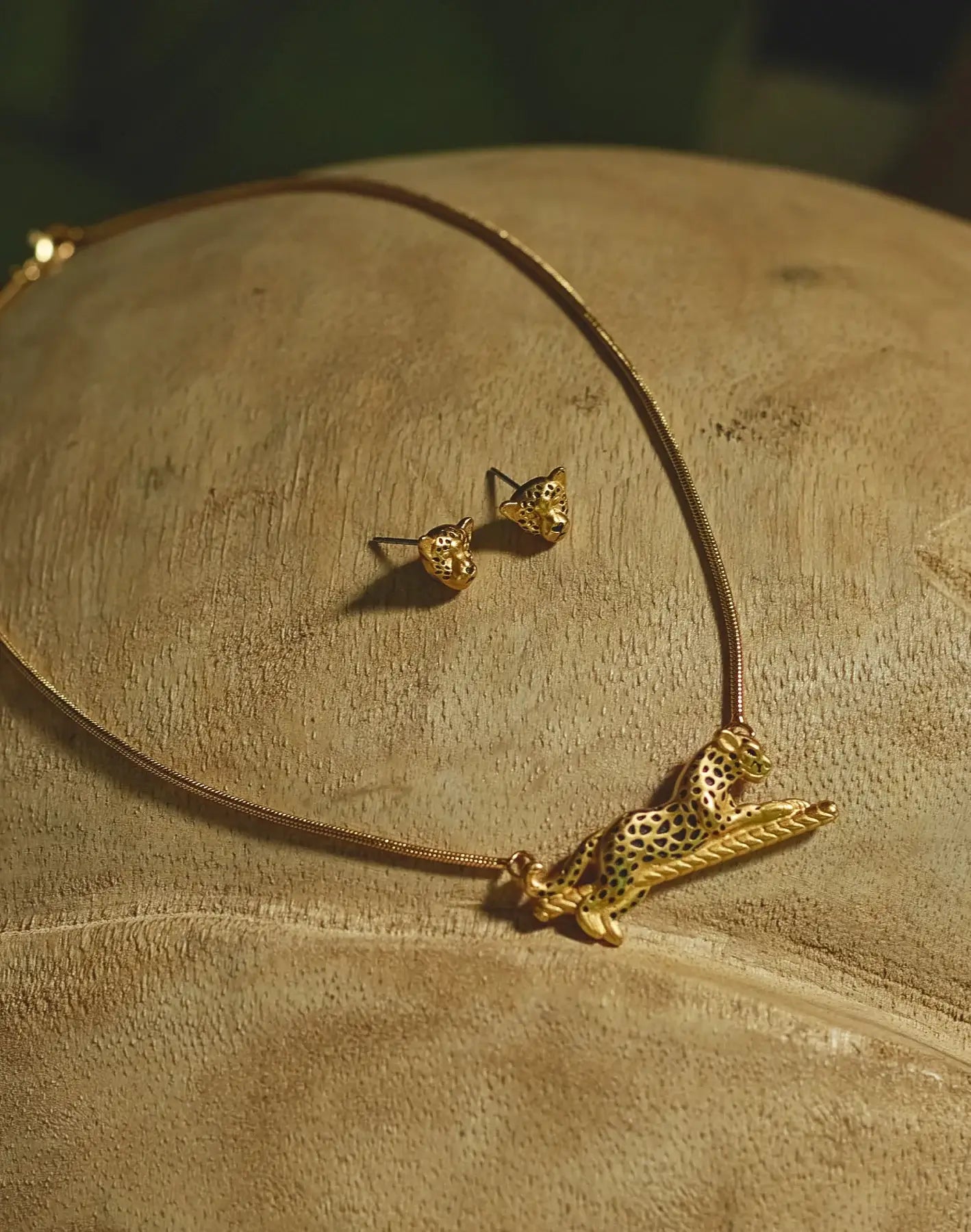 A close-up of gold-plated jaguar necklace and earrings set, placed on a wooden surface.