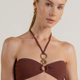 Woman wearing a brown halter bikini top with statement gold circles on a white background.