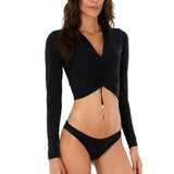 Woman wearing a black rashguard and swimsuit bottoms. She's standing against a white background. The purpose of this image is to highlight the swimsuit.