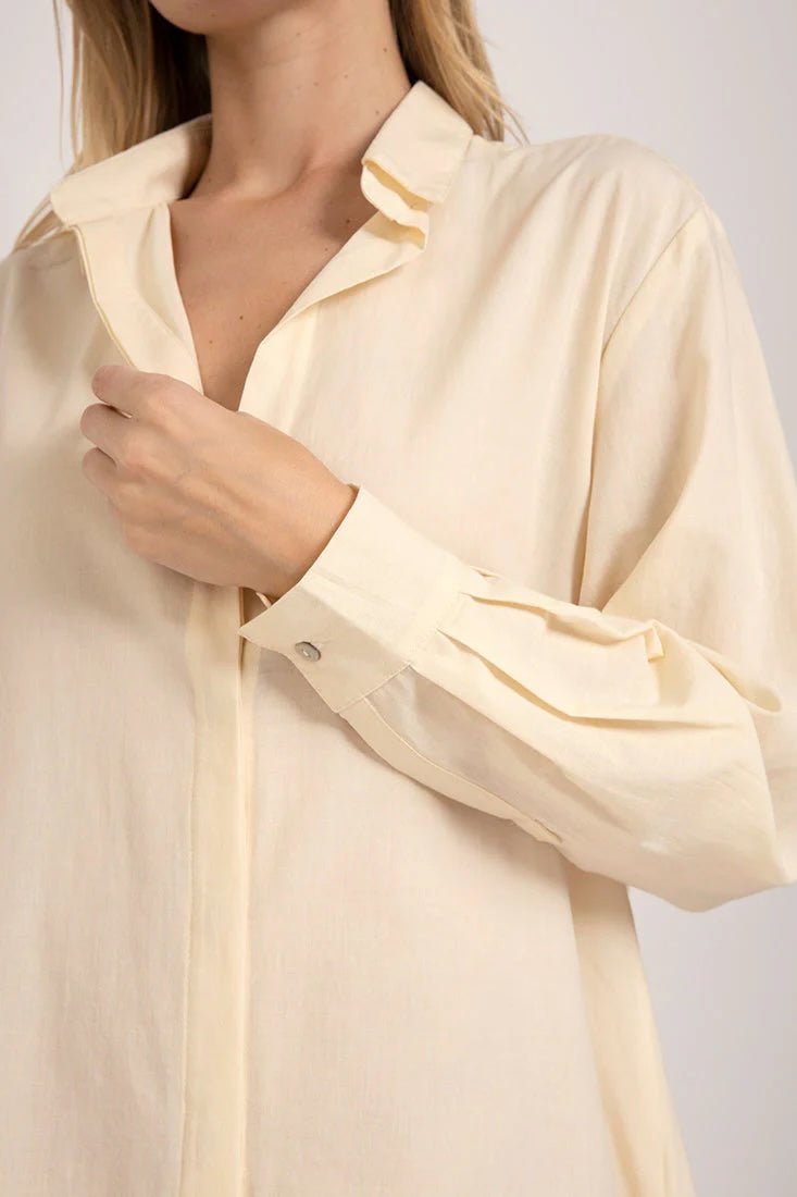 Close up image of a woman an ivory button down shirt. She's standing against a white background. The purpose of this image is to highlight the shirt.