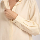 Close up image of a woman an ivory button down shirt. She's standing against a white background. The purpose of this image is to highlight the shirt.