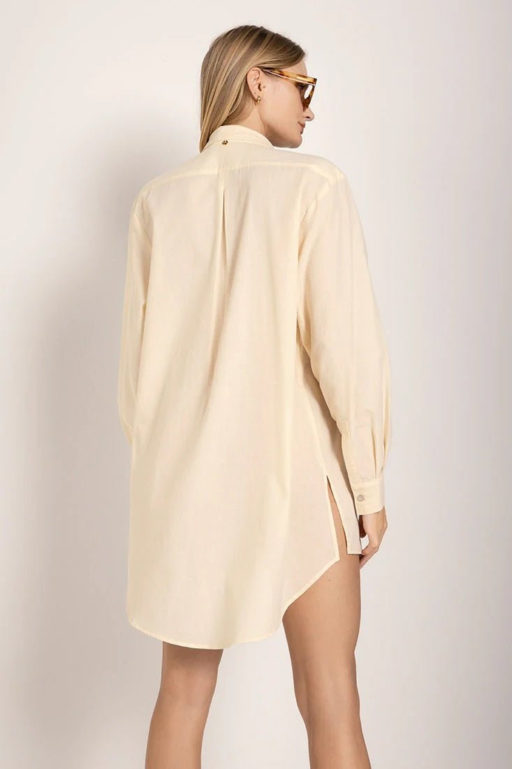 Image of a woman wearing sunglasses and an ivory button down shirt. She's giving the viewer her back and looking to the side. She's against a white background. The purpose of this image is to highlight the shirt.