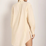 Image of a woman wearing sunglasses and an ivory button down shirt. She's giving the viewer her back and looking to the side. She's against a white background. The purpose of this image is to highlight the shirt.