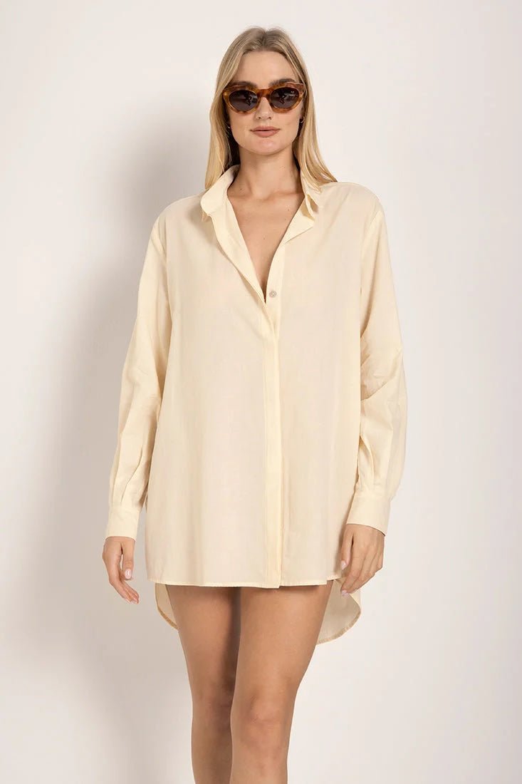 Image of a woman wearing sunglasses and an ivory button down shirt. She's standing against a white background. The purpose of this image is to highlight the shirt.