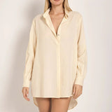 Image of a woman wearing sunglasses and an ivory button down shirt. She's standing against a white background. The purpose of this image is to highlight the shirt.