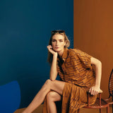 Image of a woman wearing sunglasses on top of her head and an embroidered set. She is sitting against a brown and blue background. She's looking at the camera. The purpose of this image is to highlight the skirt and shirt.