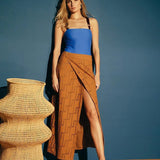 Image of a woman wearing an embroidered skirt over her swimsuit. She is standing against a blue wall and looking at the camera. The purpose of this image is to highlight the skirt.