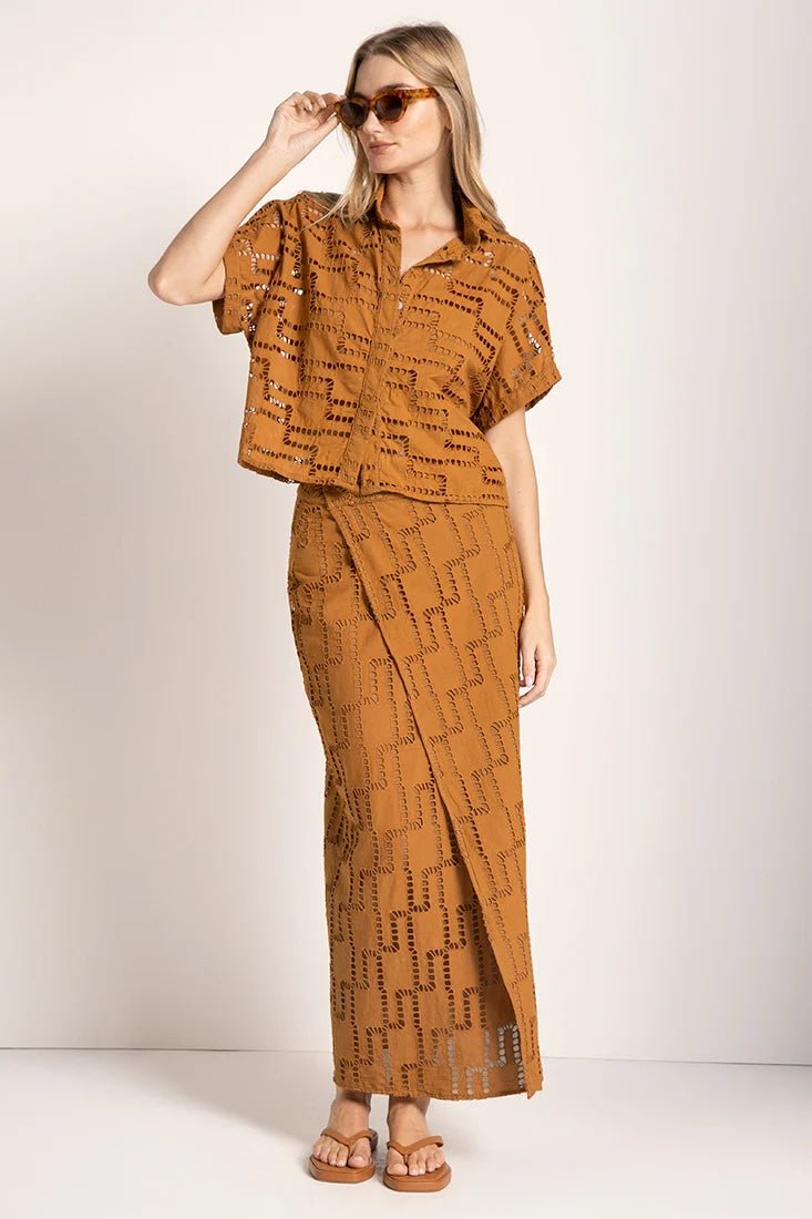 Image of a woman wearing sunglasses and an embroidered set. She is looking to the side. The purpose of this image is to highlight the skirt and shirt.