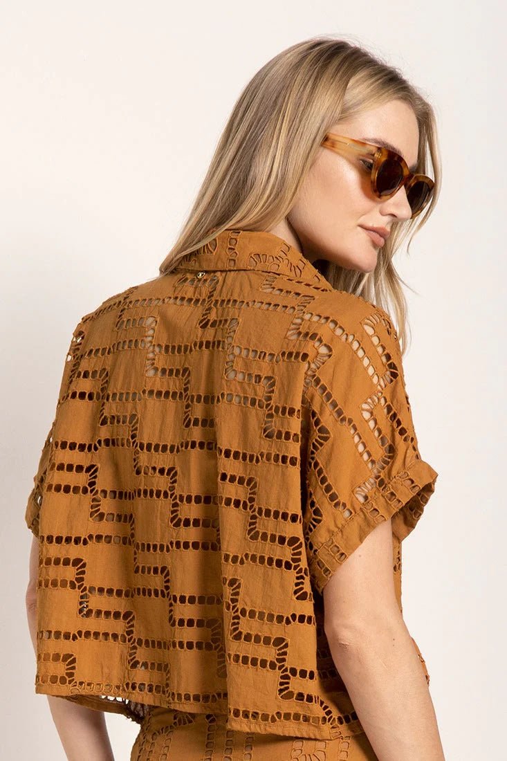 Close up image of a woman wearing sunglasses and an embroidered shirt. She's against a white background. The purpose of this image is to highlight the shirt.