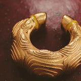 A gold-plated earcuff with a textured forest-inspired design, displayed on a dark surface.