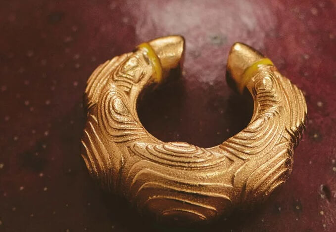 A gold-plated earcuff with a textured forest-inspired design, displayed on a dark surface.