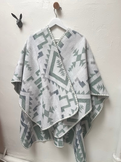 Gray, green and white geometric patterned poncho draped over a hanger against a white wall.