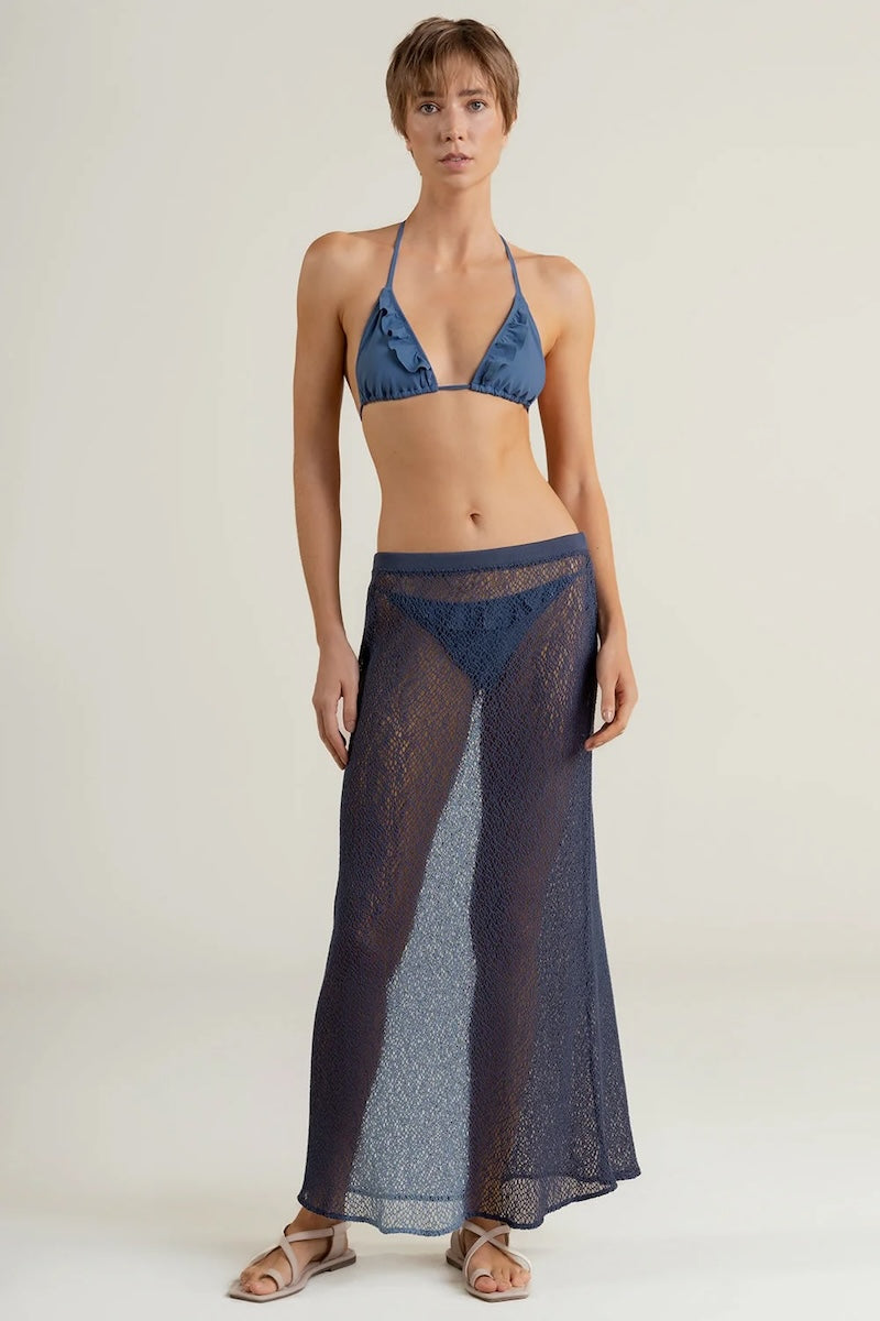 Woman wearing a blue bikini with a matching long sheer maxi skirt on a plain background.
