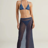 Woman wearing a blue bikini with a matching long sheer maxi skirt on a plain background.