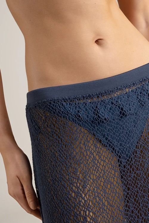 Close-up of a navy blue fishnet maxi skirt worn by a person on a beige background.