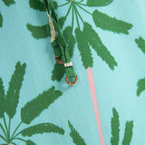Close up image of a woman wearing a long cover-up dress with a green and blue palm tree print. This close-up just shows the straps, which have a gold detail on the end. The purpose of this image is to highlight the dress.