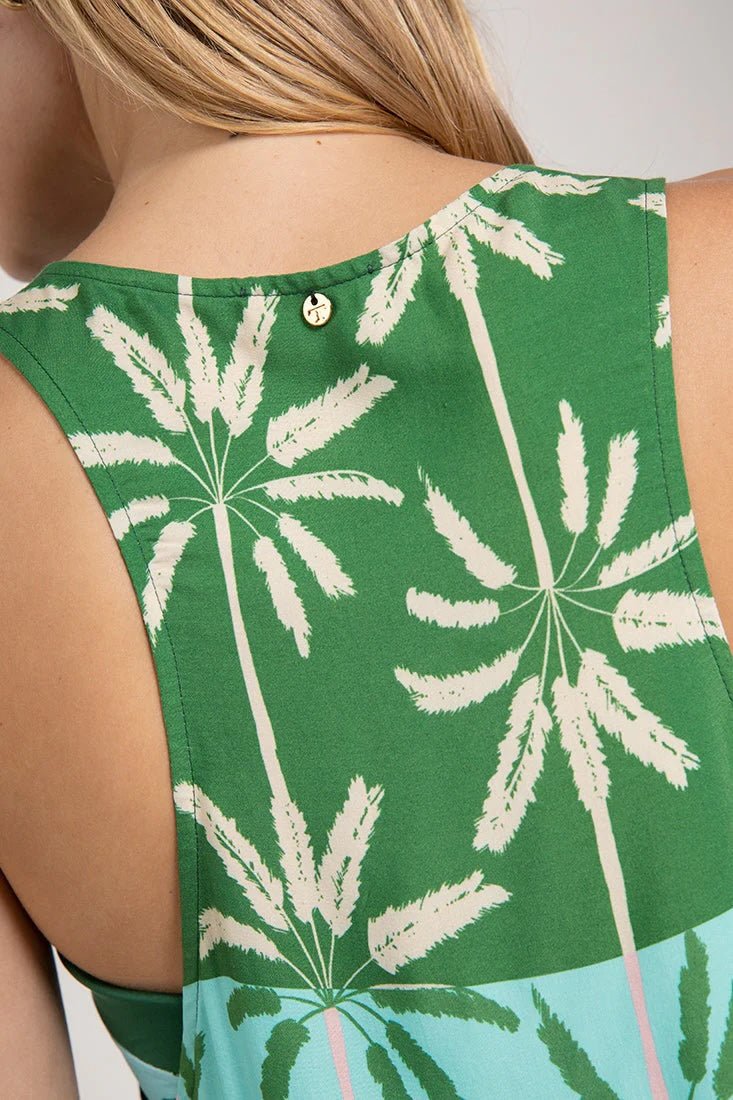 Close up image of a woman wearing a sleeveless cover-up dress with a green and blue palm tree print. She's looking to the side and standing in front of a white background. The purpose of this image is to highlight fit on the back of the dress.