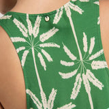 Close up image of a woman wearing a sleeveless cover-up dress with a green and blue palm tree print. She's looking to the side and standing in front of a white background. The purpose of this image is to highlight fit on the back of the dress.