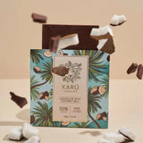 A chocolate bar with coconut milk and '50% CACAO' text on it, with palm trees on the packaging. Coconut pieces are scattered around, and the bar has a sticker with the brand 'Karü'.